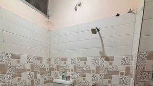 Uma casa de banho com sanita, chuveiro e porta-papel higiénico.