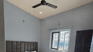 Quarto com cama, ventoinha no teto, janela com grades e guarda-roupa.