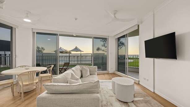 A spacious living room with a large sofa, a coffee table, and a TV mounted on the wall. - Absolute Beachfront Apartment with Direct Pool & Beach Access (Main Beach)