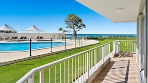 A poolside view with a clear blue sky, a tree, and a view of the ocean. - Absolute Beachfront Apartment with Direct Pool & Beach Access (Main Beach)