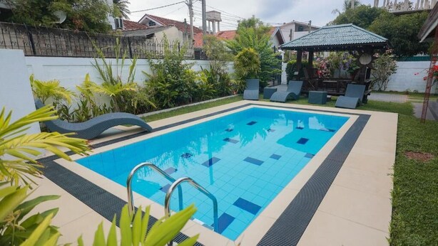 Una piscina rectangular con solárium alicatado, rodeada de follaje y un pabellón.