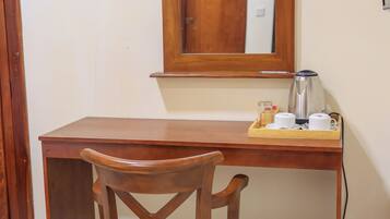 A wooden desk with a chair, a mirror, a kettle, and a trash can.