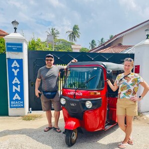 A red auto-rickshaw parked in front of a gate labeled 'AYANA BEACH GARDEN.' - Ayana Beach Garden (Negombo)