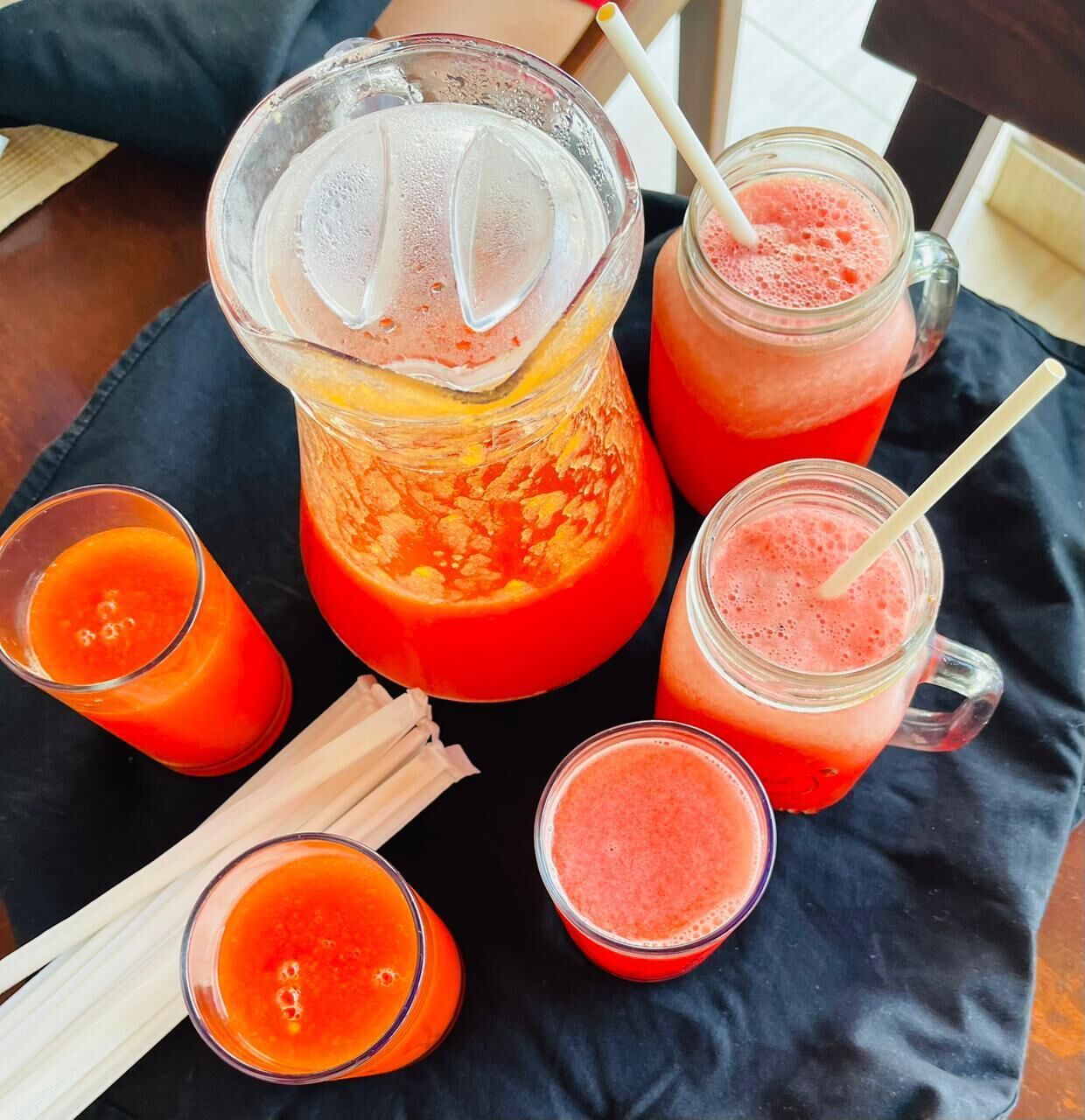 Ein Krug und mehrere Gläser mit einem roten Getränk, wahrscheinlich Fruchtsaft oder Smoothie, auf einer schwarzen Tischdecke.