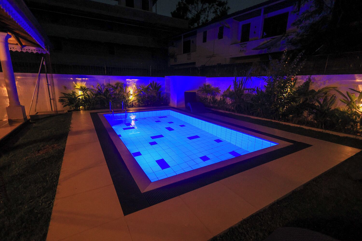 Una piscina con illuminazione blu, circondata da un'area pavimentata e piante.