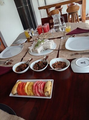 Mesa de jantar posta com pratos, tigelas de comida, jarra, copos e um prato de frutas com bananas.