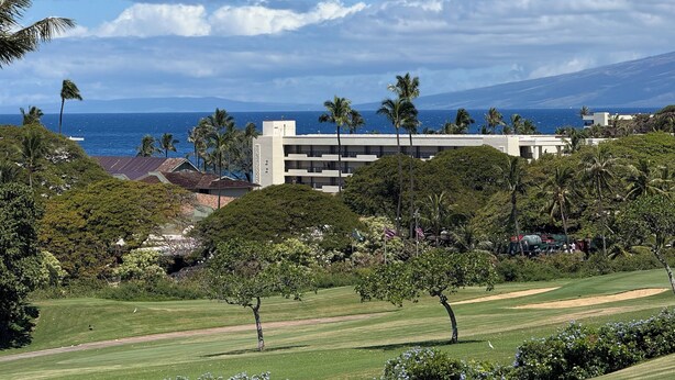 Ein Golfplatz mit Blick auf den Ozean und einem Gebäude im Hintergrund.