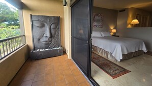 Ein Balkon mit einer großen Skulptur, ein Bett mit weißer Bettdecke und ein Nachttisch mit Lampe.