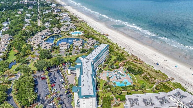 An aerial view of a coastal hotel with multiple swimming pools, a beach, and a parking area. - Oceanfront Luxury 2BR Litchfield Beach Escape (Pawleys Island)