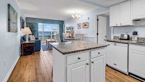 A modern kitchen with white cabinetry, a granite countertop, and a dining area with a view. - Oceanfront Luxury 2BR Litchfield Beach Escape (Pawleys Island)