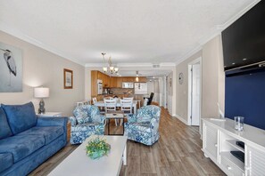 A living room with a blue sofa, patterned armchairs, a coffee table with a plant, a dining area with a white table and chairs, and a kitchen in the background. - Beach Lover's Retreat 3BR North Myrtle Beach Gem (North Myrtle Beach)
