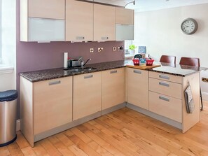 A modern kitchen with built-in cabinets, a granite countertop, a sink, and a clock on the wall.