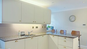 Una cucina moderna con mobili bianchi, piani di lavoro in granito, un lavello e un orologio a parete.