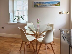 A dining area with a glass table, white chairs, a potted plant, and a painting on the wall. - 4 bedroom accommodation in Inverkip, near Greenock (Inverkip, near Greenock)