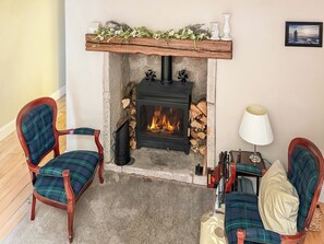 A cozy room with a fireplace, two plaid chairs, a table with a lamp, and a framed picture on the wall. - 4 bedroom accommodation in Inverkip, near Greenock (Inverkip, near Greenock)