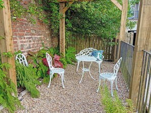 A garden patio with white metal furniture, a brick wall, and a wooden pergola. - 4 bedroom accommodation in Inverkip, near Greenock (Inverkip, near Greenock)