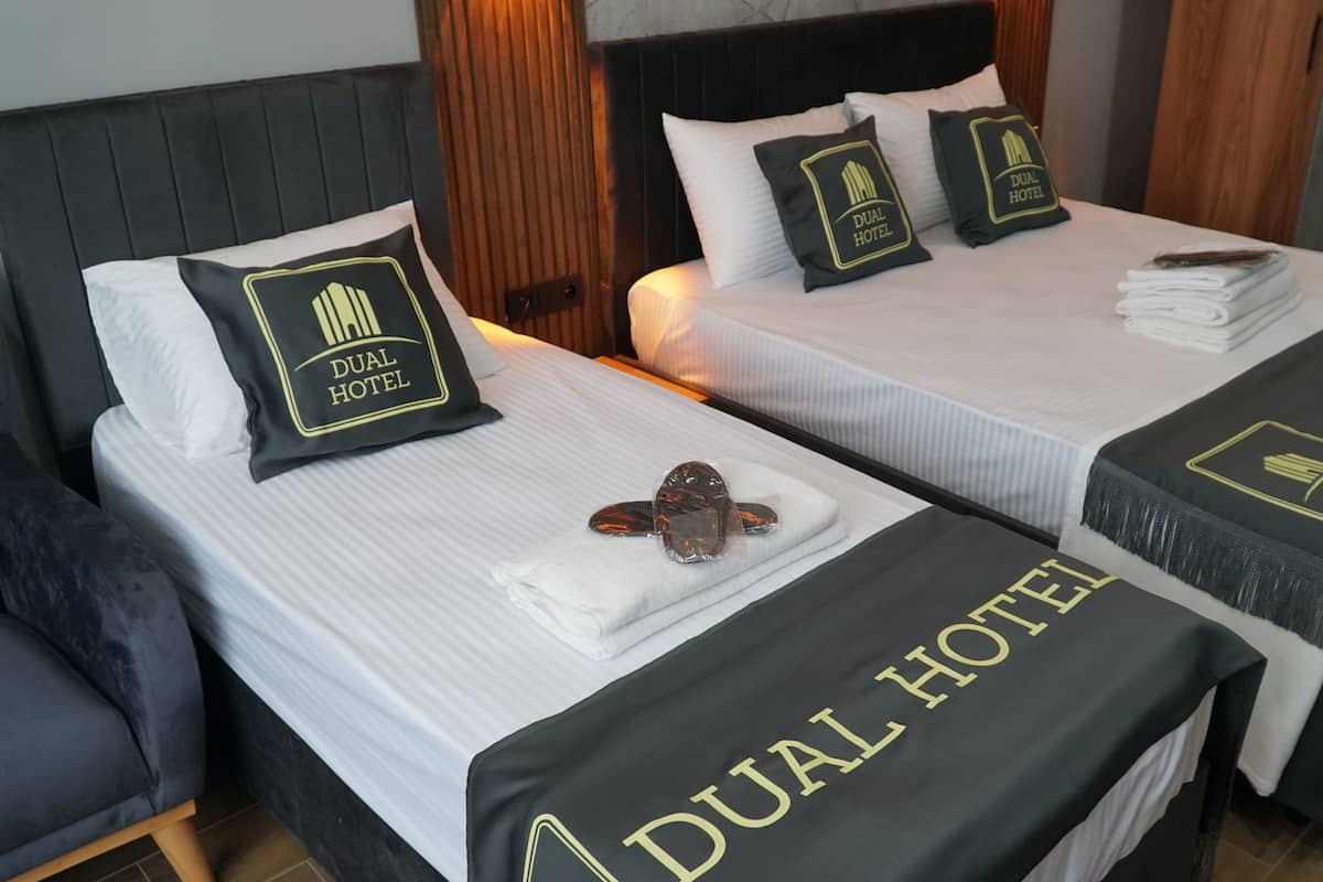 Two twin beds with "Dual Hotel" branding, white linens, and a heart-shaped decoration on the left bed.