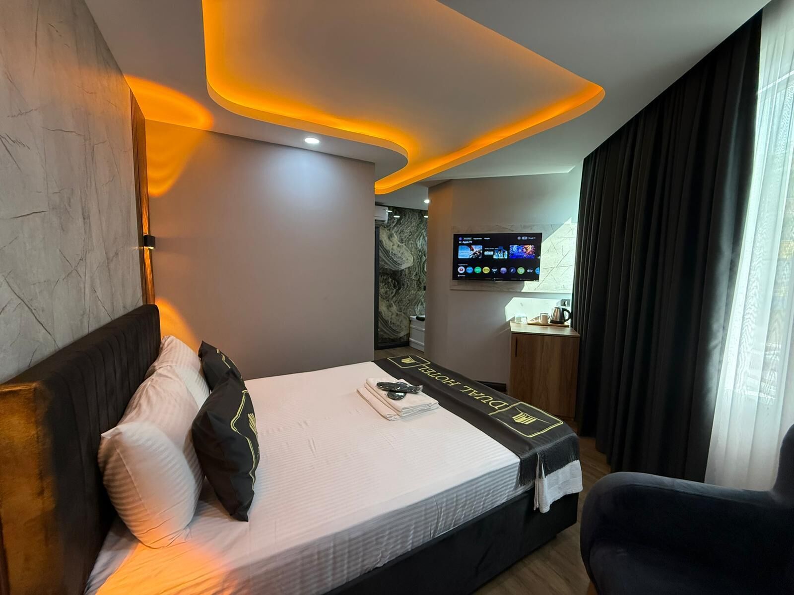 A modern hotel room with a neatly made bed, a television mounted on the wall, and a small table with a coffee maker.