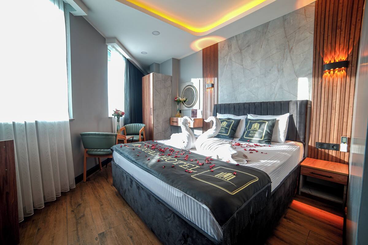 A modern hotel room with a large bed, a wooden nightstand, a chair, and a mirror.