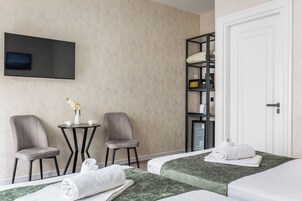 Hotellihuone, jossa on kaksi sänkyä, pieni pöytä tuoleineen, seinälle asennettu televisio ja hylly, jossa on erilaisia tavaroita.