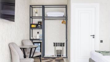 Quarto de hotel compacto com cama, área de estar com mesa e cadeiras, nicho embutido com artigos de higiene e uma porta.