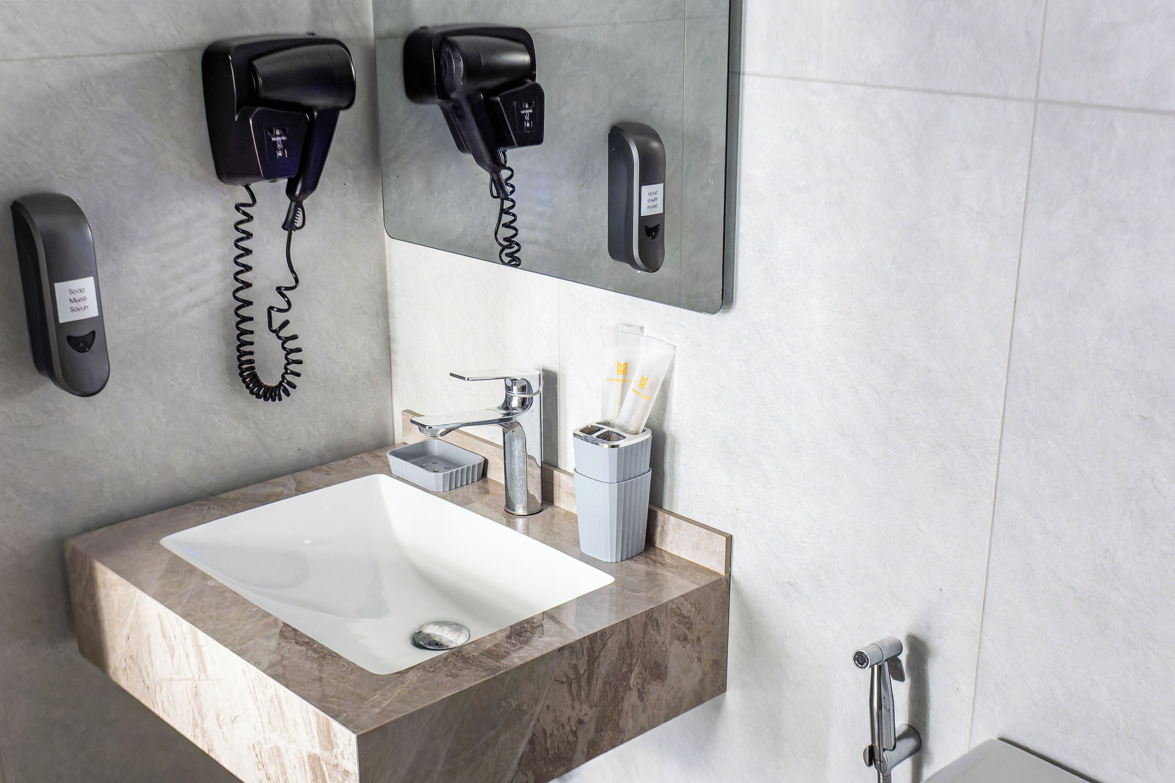 A bathroom with a marble sink, a mirror, a hairdryer, and a hand dryer mounted on the wall.