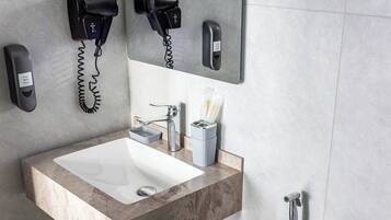 A bathroom with a marble sink, a mirror, a hairdryer, and a hand dryer mounted on the wall.