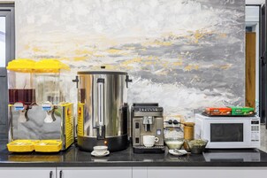 Una encimera de cocina con una cafetera, una jarra de café, un dispensador de jugo y un microondas.