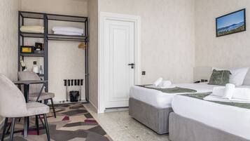 A hotel room with two beds, a desk, a chair, a radiator, and a painting on the wall.