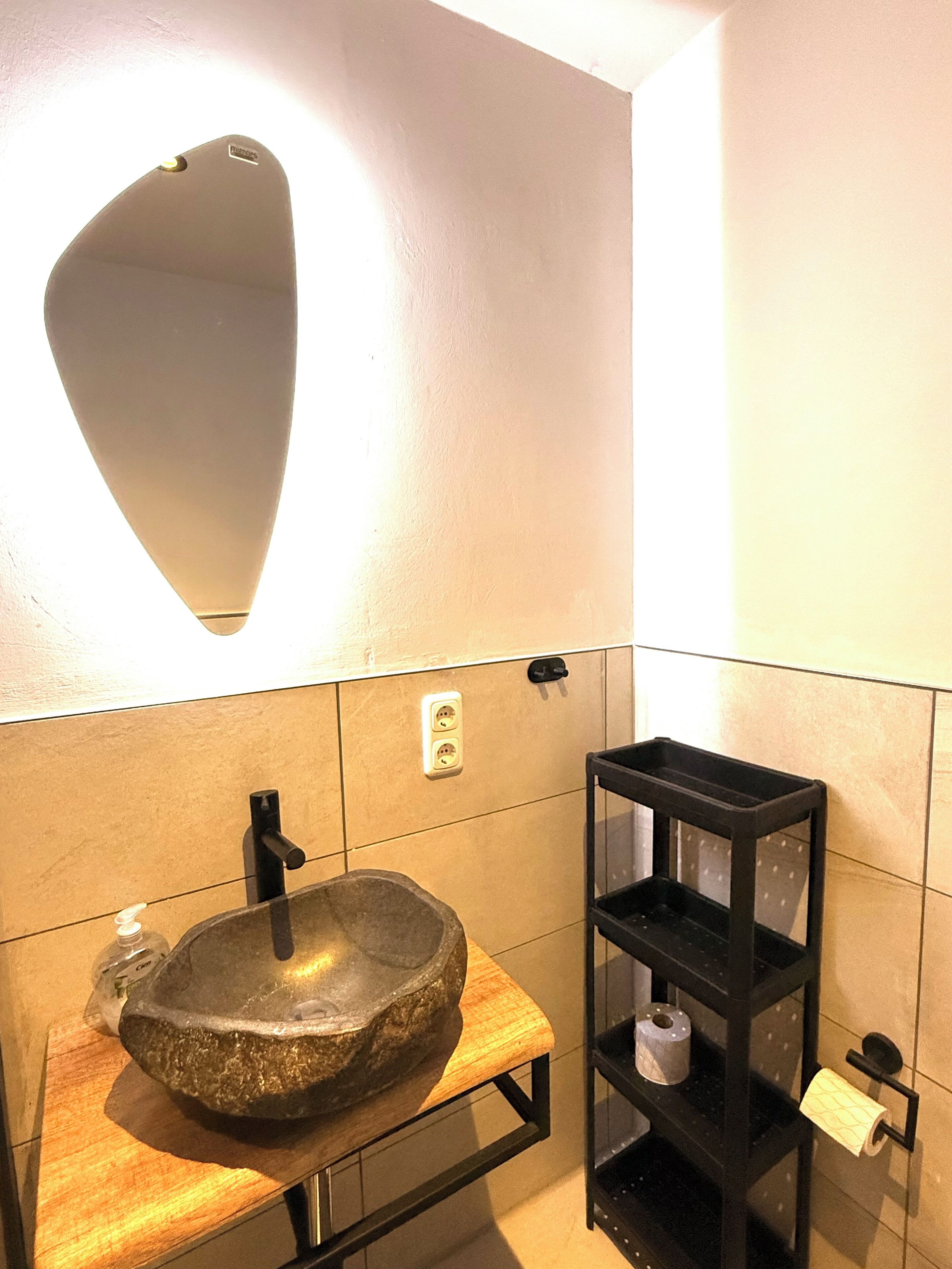 A bathroom with a stone sink, a mirror, a shelf with toiletries, and a towel rack.