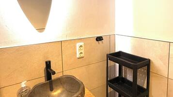 A bathroom with a stone sink, a mirror, a shelf with toiletries, and a towel rack.
