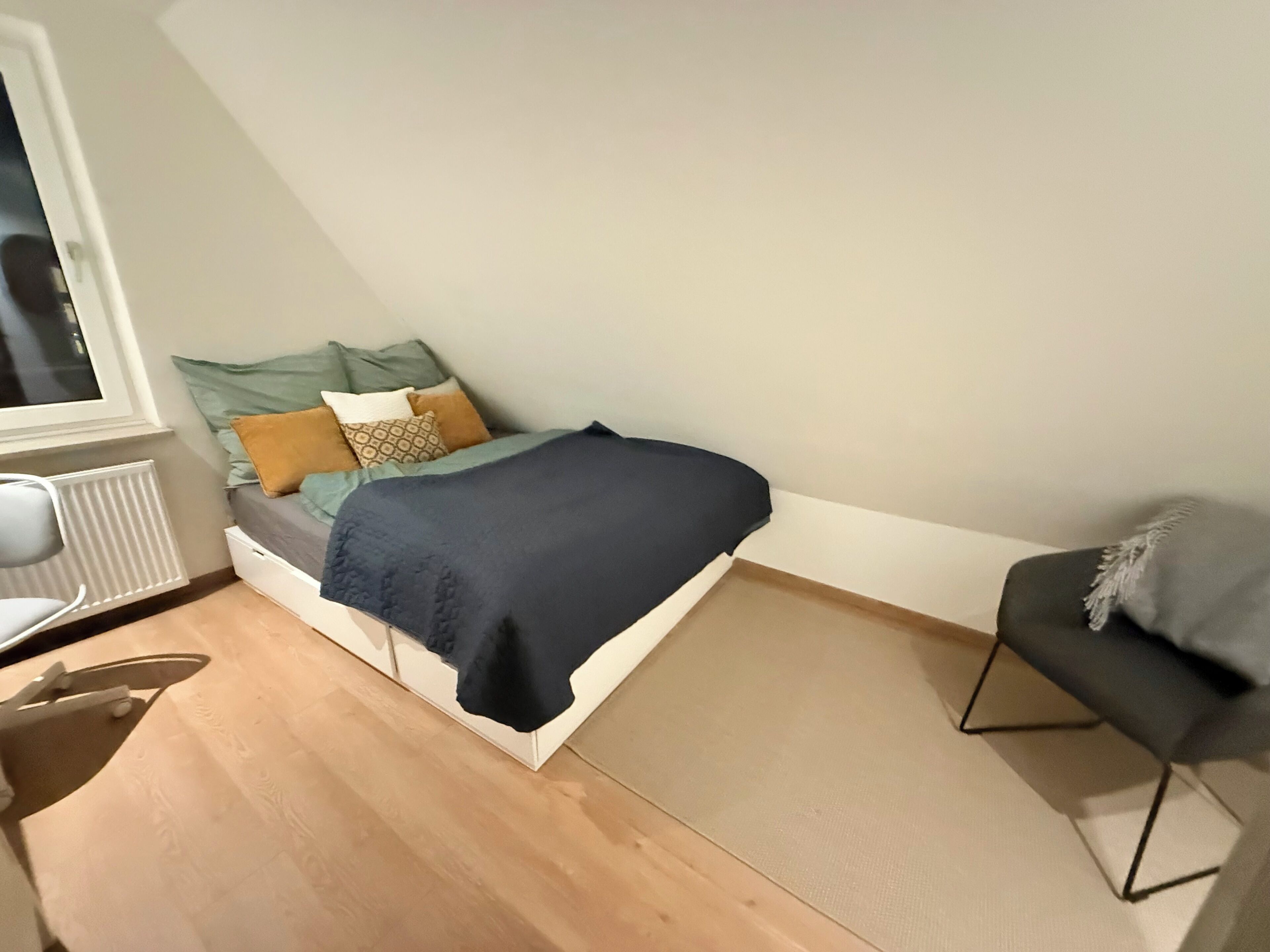 Een kleine, knusse kamer met een bed, een stoel en een radiator.