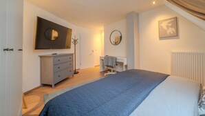 Ein Schlafzimmer mit Bett, Schreibtisch, Kommode und einem großen Spiegel an der Wand.