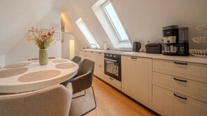 Eine moderne Küche mit Oberlichtern, einem Essbereich mit rundem Tisch und Stühlen sowie einer Kaffeemaschine.