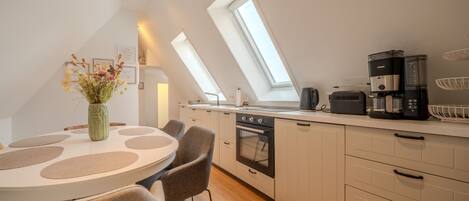 A modern kitchen with skylights, a dining area with a round table and chairs, and a coffee maker.