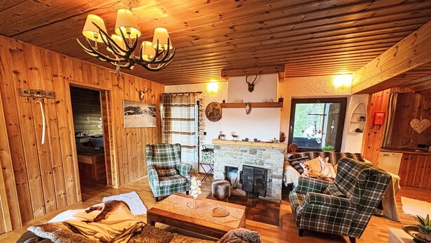 Ein gemütliches Blockhaus-Interieur mit Kamin, Karo-Möbeln und Holzbalkendecke.