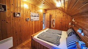 Ein gemütliches Schlafzimmer einer Holzhütte mit Bett, Nachttisch, Spiegel und einem gerahmten Bild an der Wand.