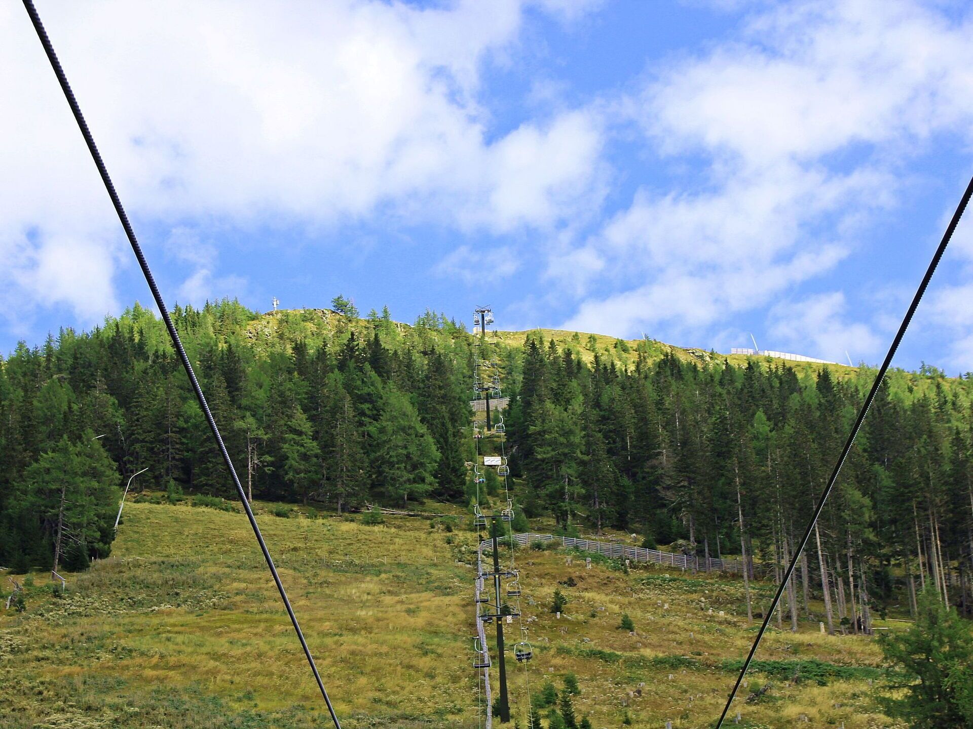A mountain landscape with a ski lift, forested slopes, and a clear sky.