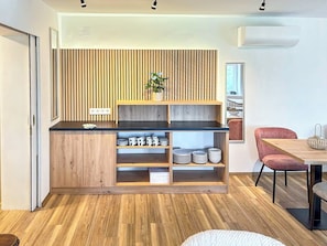 Eine moderne Küche mit Holzschränken, einer schwarzen Arbeitsplatte und einer eingebauten Regaleinheit mit Tellern und Tassen.