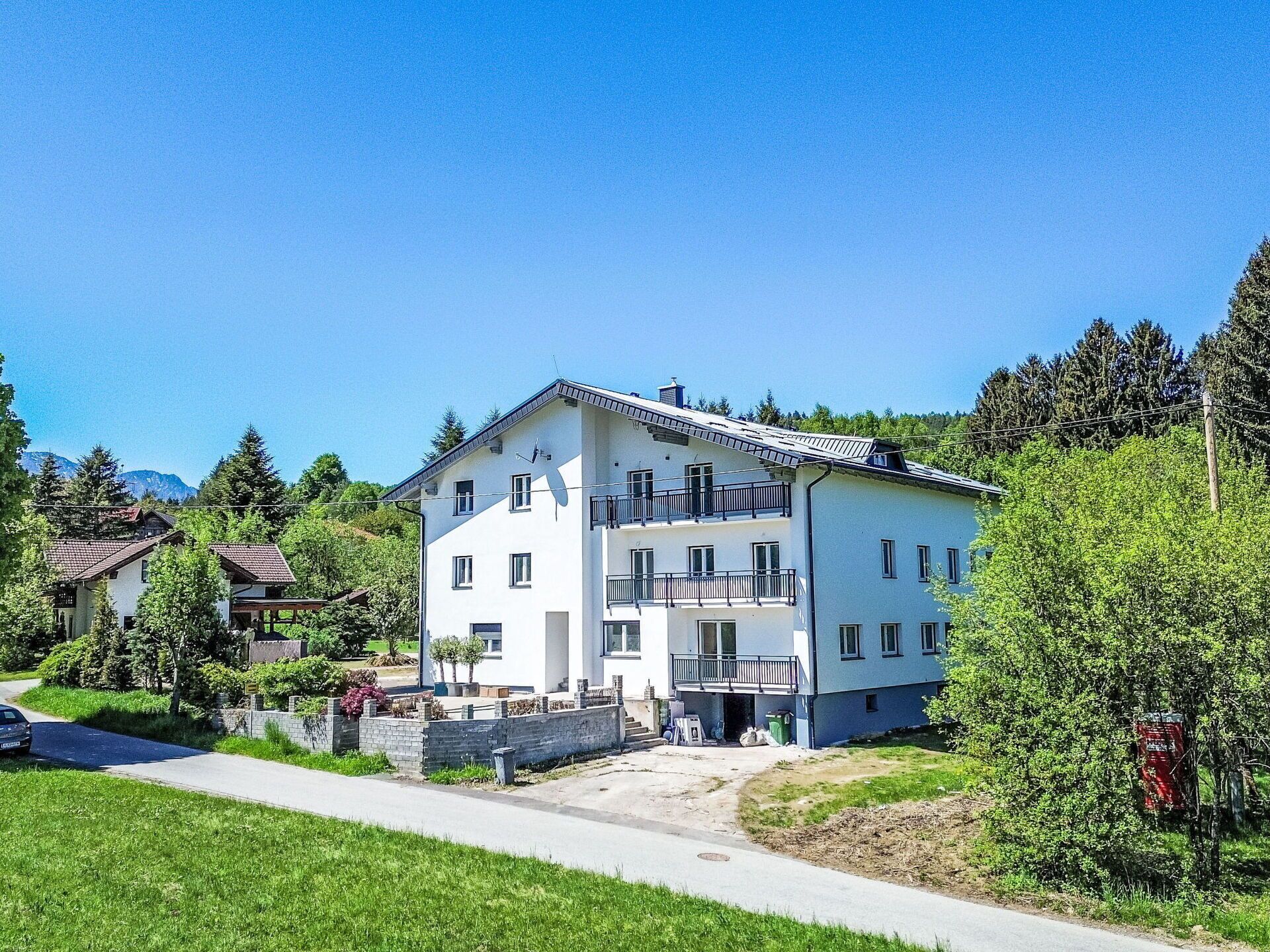 A multi-story building with a balcony, surrounded by greenery and a clear sky.