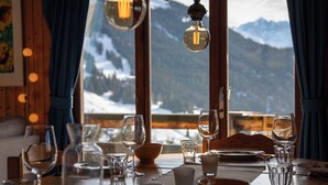 Een eettafel gedekt met glazen en borden, met uitzicht op een besneeuwd berglandschap door grote ramen.