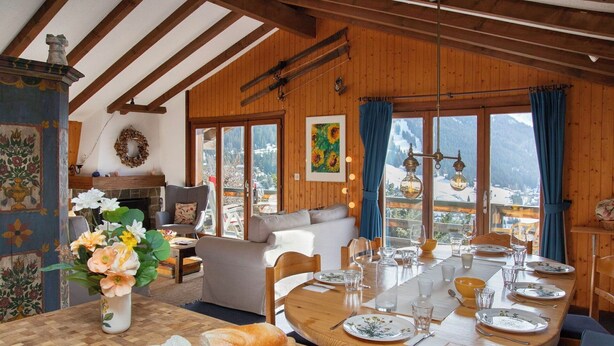 Een eetgedeelte met een houten tafel gedekt voor vier personen, een open haard en uitzicht op een besneeuwde berg.