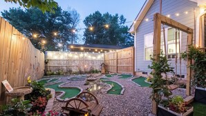 Um quintal com um campo de mini golfe, cerca de madeira e luzes de corda.
