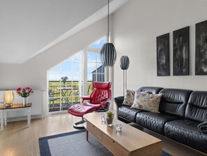 A modern living room with a black leather sofa, a red chair, a wooden coffee table, and a view of a green landscape through large windows. - "Alitta" - 240m from the sea by Interhome (Bogense)