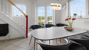 A dining area with a white table and chairs, a staircase with red accents, and a view of the countryside through large windows. - "Alitta" - 240m from the sea by Interhome (Bogense)