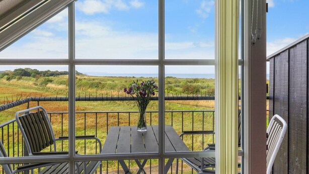 A covered patio with a table and chairs, a vase with flowers, and a view of a grassy field and trees. - "Alitta" - 240m from the sea by Interhome (Bogense)