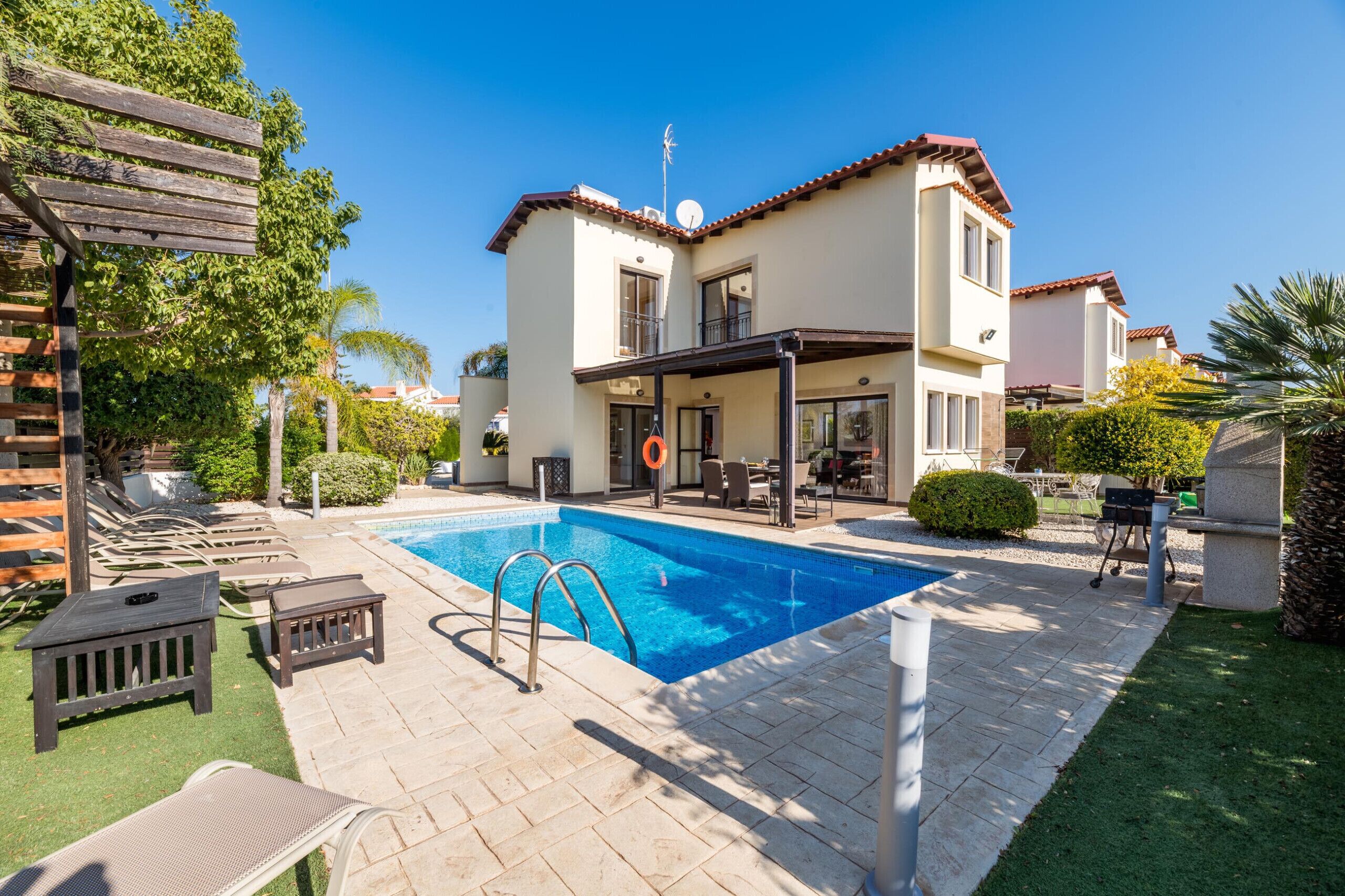 A two-story house with a swimming pool, outdoor furniture, and a pergola.
