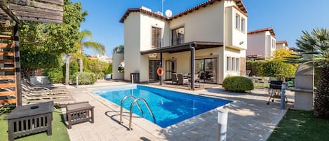 A two-story house with a swimming pool, outdoor furniture, and a pergola.