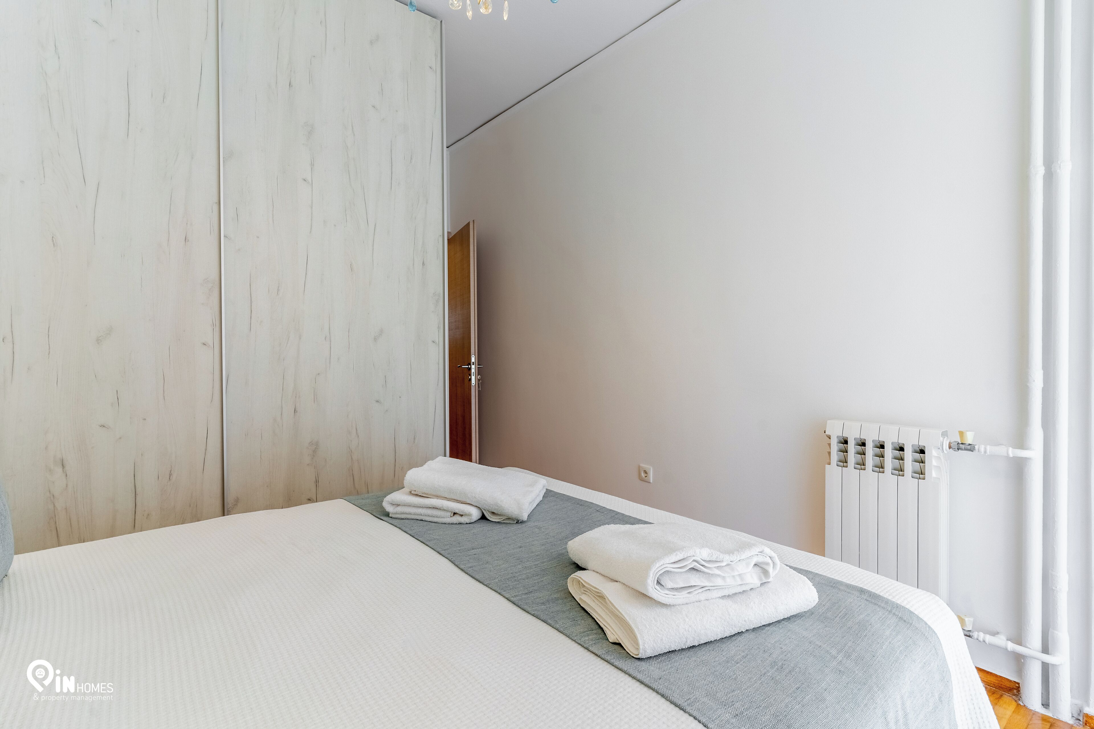 Un dormitorio con cama, un corredor de cama gris y toallas blancas dobladas con cuidado.