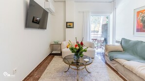 Un salon moderne avec une table basse en verre, un canapé, un téléviseur fixé au mur et une vue sur l’extérieur.
